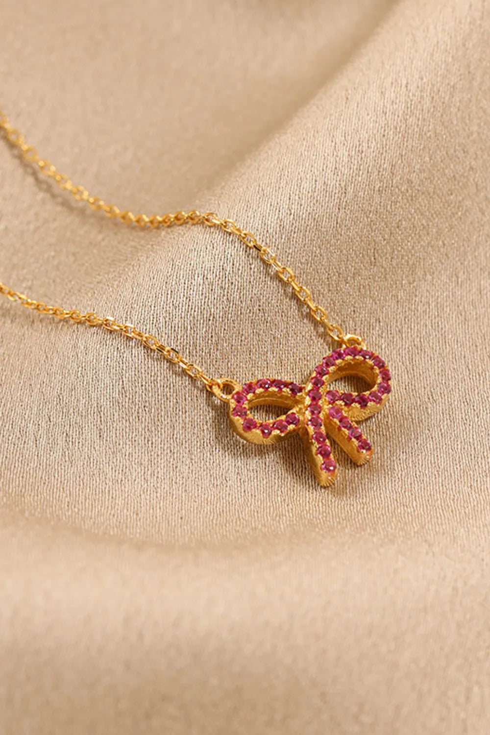 A gold chain with a gold bow pendant set with red stones
