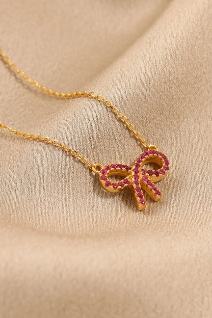 A gold chain with a gold bow pendant set with red stones