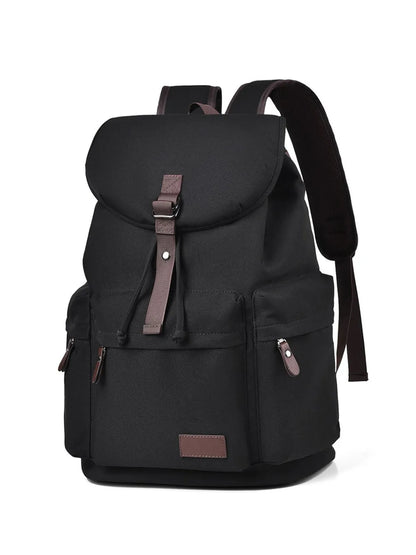 Front view of a black backpack made with canvas material. There are two lower side pockets, one on either side, and another pocket on the front. There is a large flap on the top and front, covering the main compartment of the bag. Zip tags and trimmings are coffee brown.