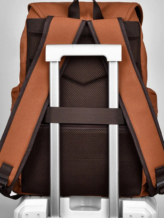 Back view of a brown backpack sitting on a suitcase, showing the bag straps and back padding. The extendable handle of the suitcase has been passed through a horizontal strap on the back of the bag.