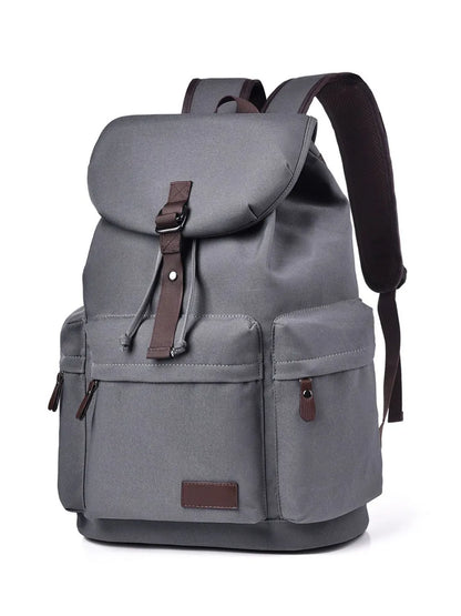 Front view of a grey backpack made with canvas material. There are two lower side pockets, one on either side, and another pocket on the front. There is a large flap on the top and front, covering the main compartment of the bag. Zip tags and trimmings are coffee brown.