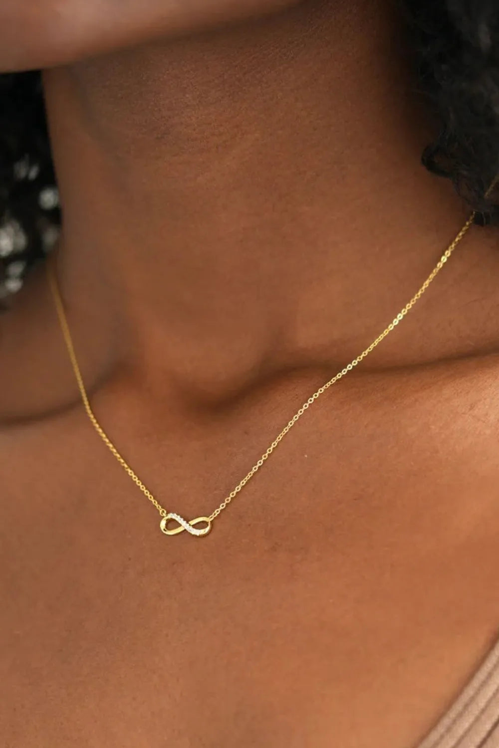 A gold-plated necklace with an infinity pendant worn on the neck of a woman. Picture is taken at an angle