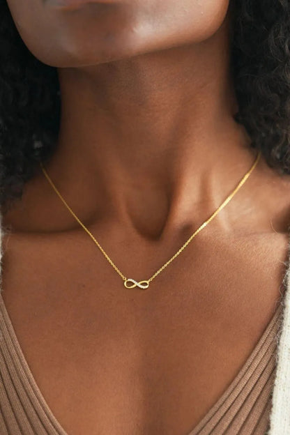 A gold-plated necklace with an infinity pendant worn on the neck of a woman