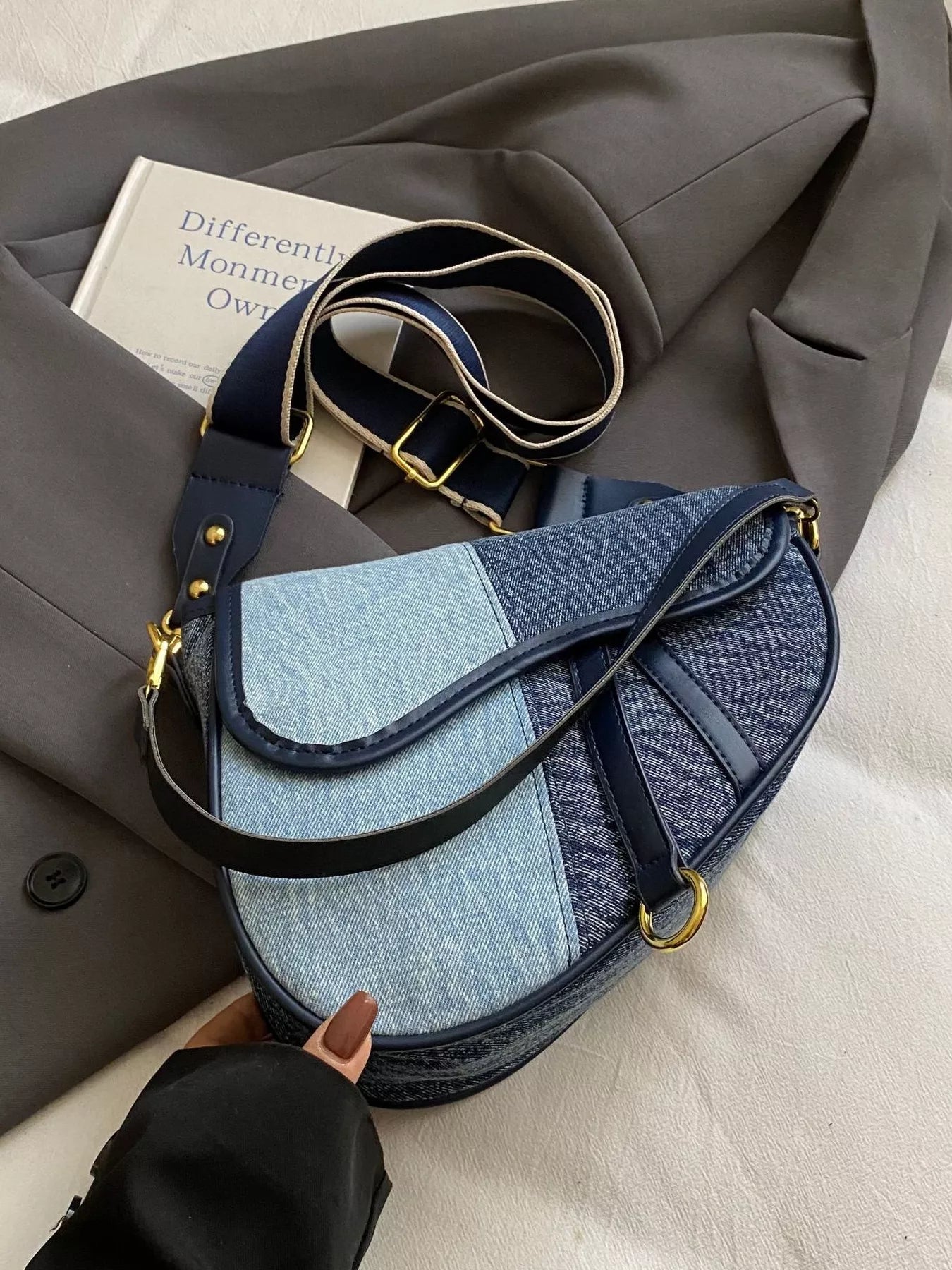 Picture of a light blue denim saddle bag on a grey blazer and cream surface