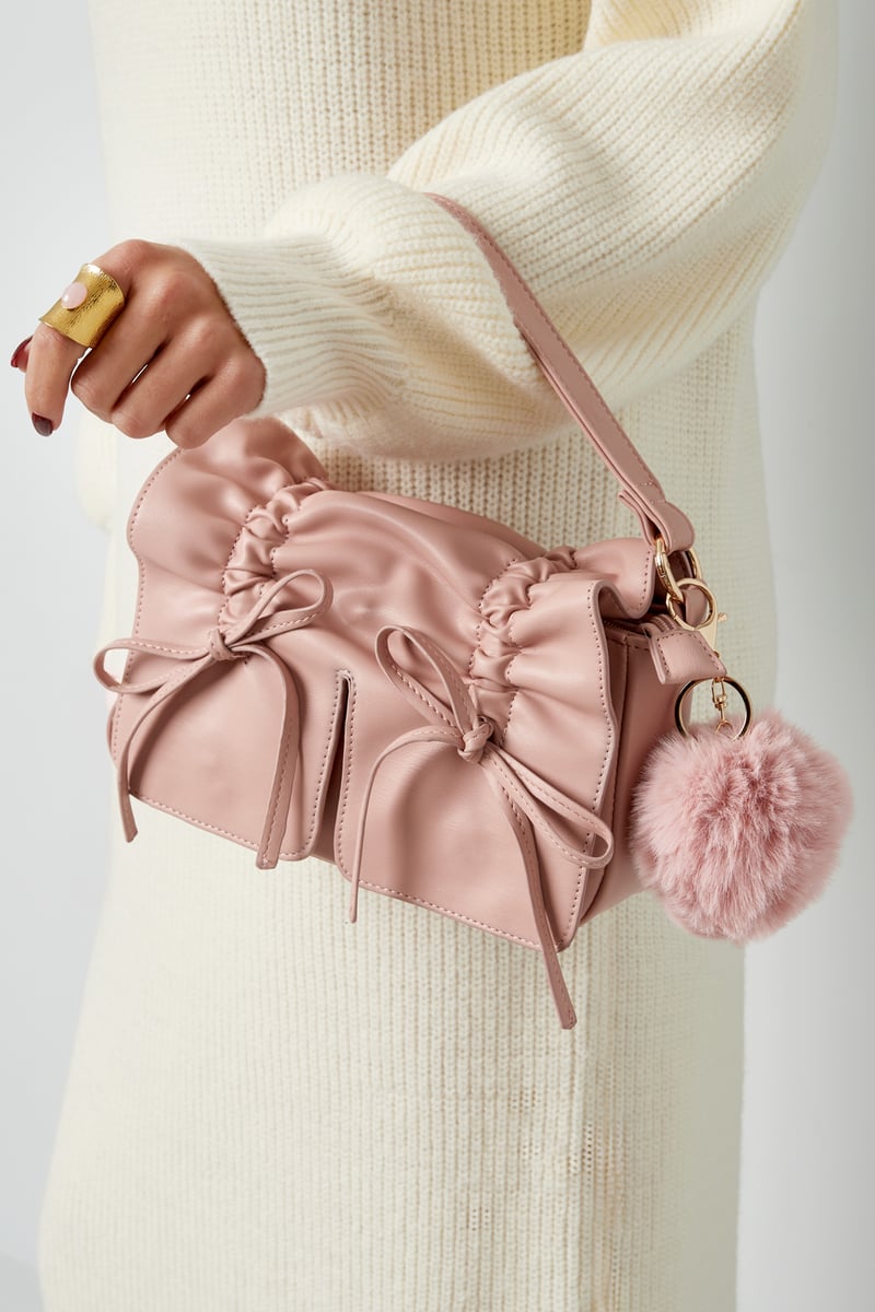 Pink Puffy Ball Keyring attached to a dusty pink handbag, hanging from the wrist of a female in a cream longsleeve dress, and gold index ring