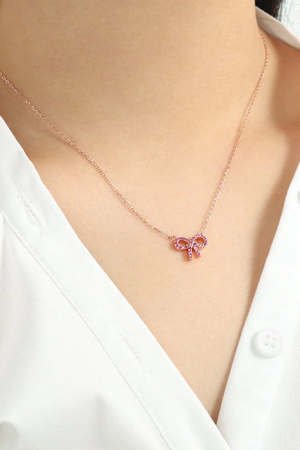 A silver chain with a rose bow pendant set with red stones on the neck of a model