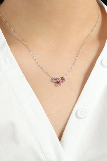 A silver chain with a silver bow pendant set with red stones on the neck of a model