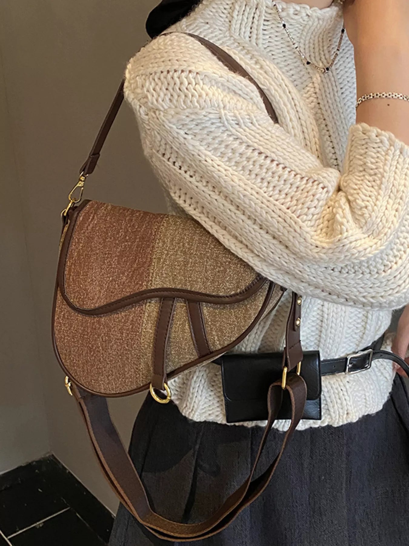 Picture of a female figure in a cream sweater and dark grey skirt, carrying a two-tone brown denim saddle bag on her shoulder