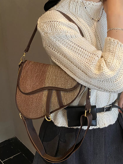 Picture of a female figure in a cream sweater and dark grey skirt, carrying a two-tone brown denim saddle bag on her shoulder